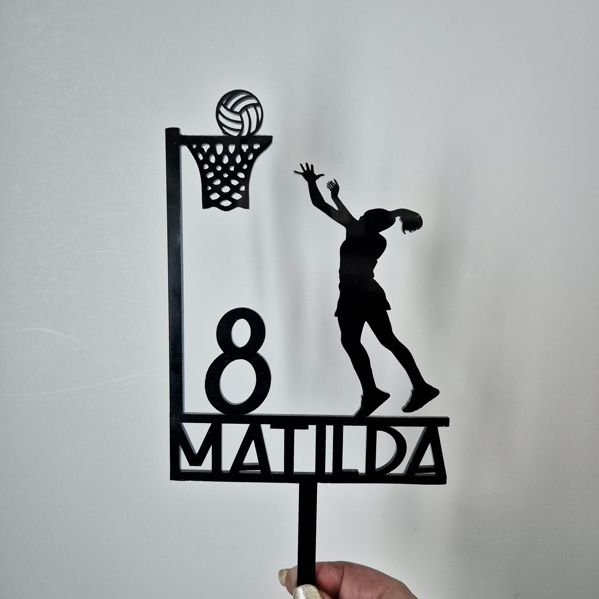 Black Cake Topper of a netball player diving with personalised name and number on a light gray background