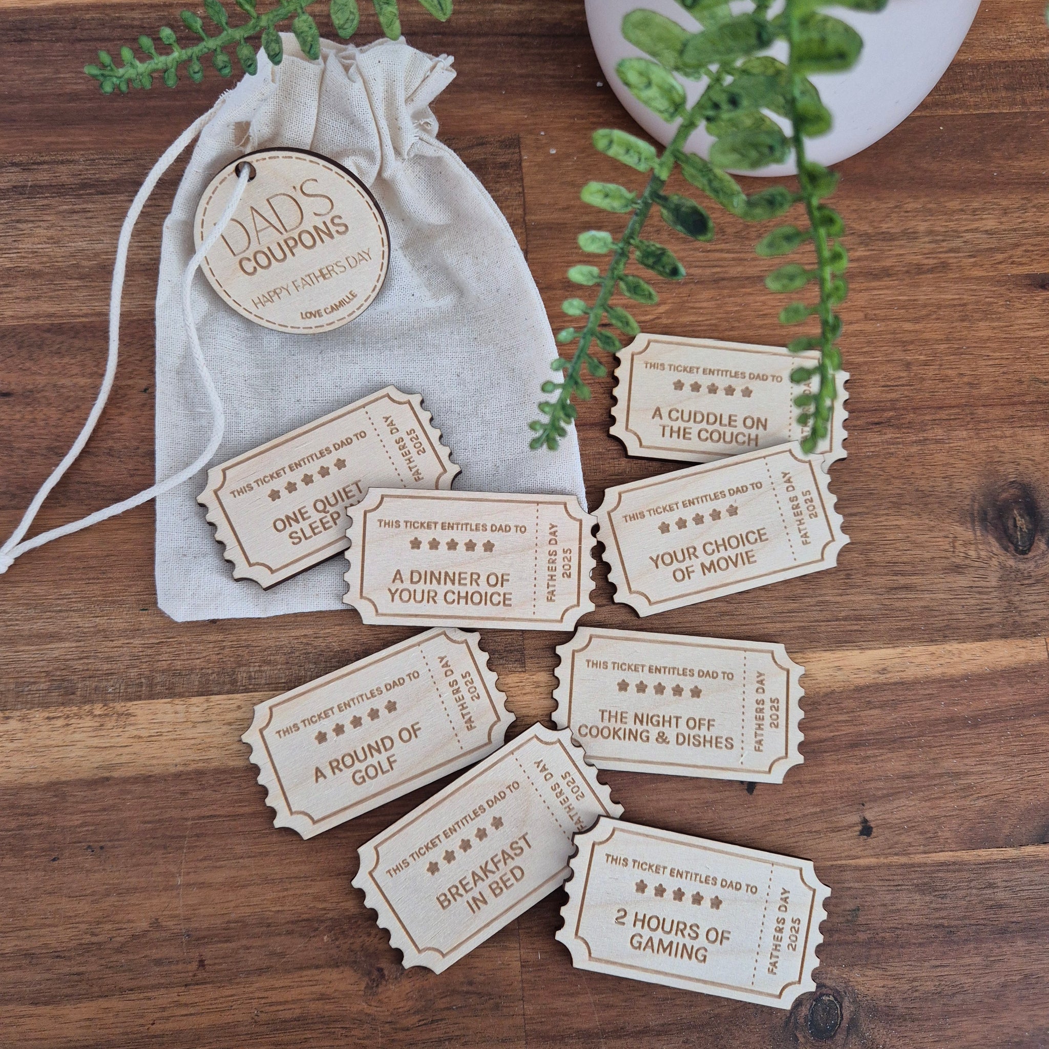 Set of wooden fathers day coupons on a wooden surface with a drawstring bag and plant leaves.