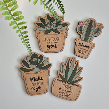 Set of wooden decorative fridge magnets with plant designs and motivational phrases on a light background.