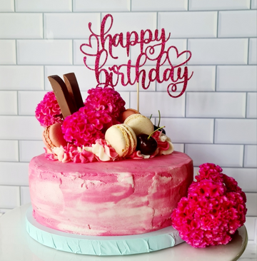 Image of a pink cake with a custom glitter cardstock cake topper saying happy birthday