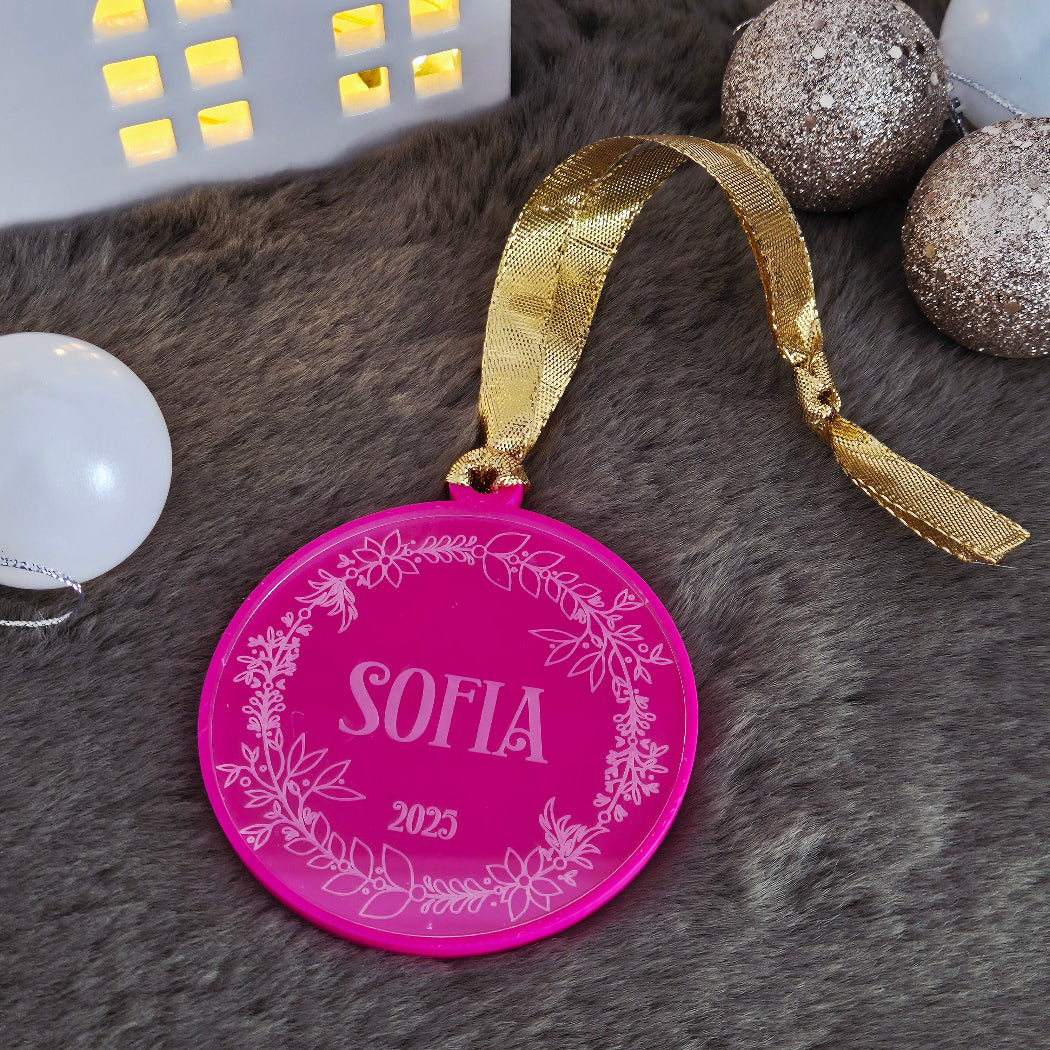 Pink ornament with gold ribbon and 'Sofia' engraving on a textured surface