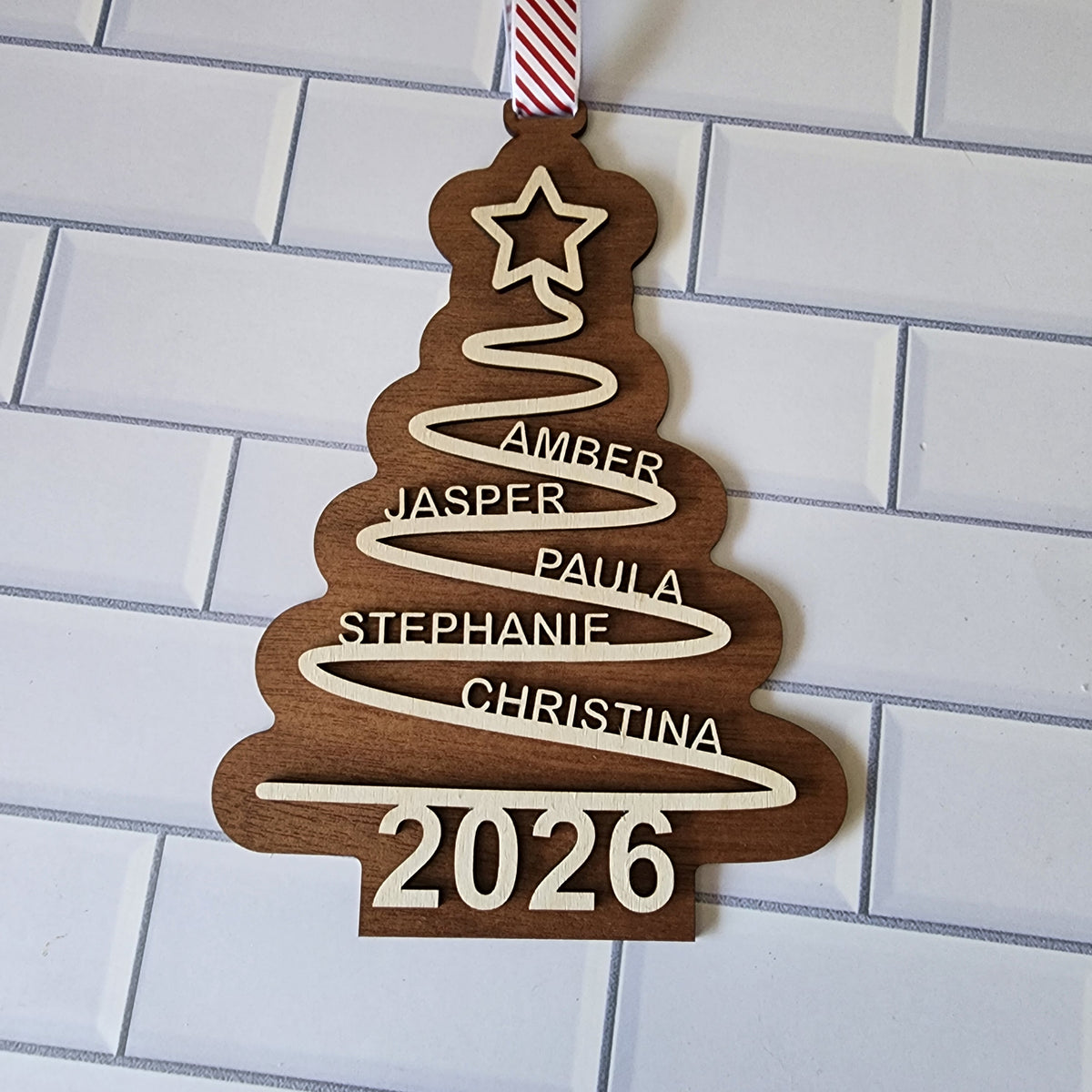 Personalised wooden family Christmas tree ornament with custom names and year 2026 hanging with red striped ribbon