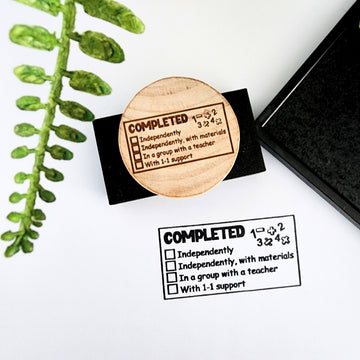 Wooden handheld teacher stamp featuring a maths theme and saying Completed independently, with materials, with a teacher with 1-1 support
