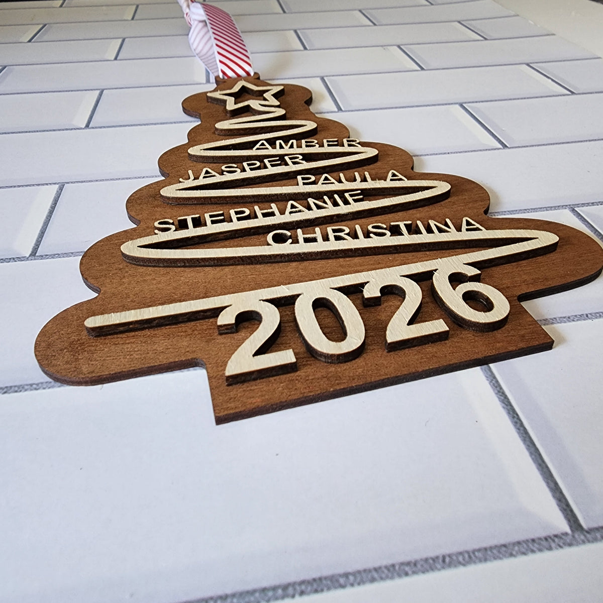 Custom wooden family Christmas tree ornament with custom names and year 2026 hanging with red striped ribbon