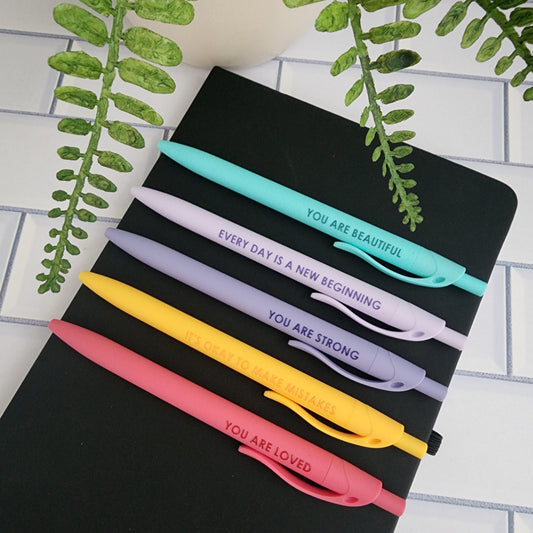 Positive Affirmation Pen Set of 5 soft touch colorful pens resting on a black journal