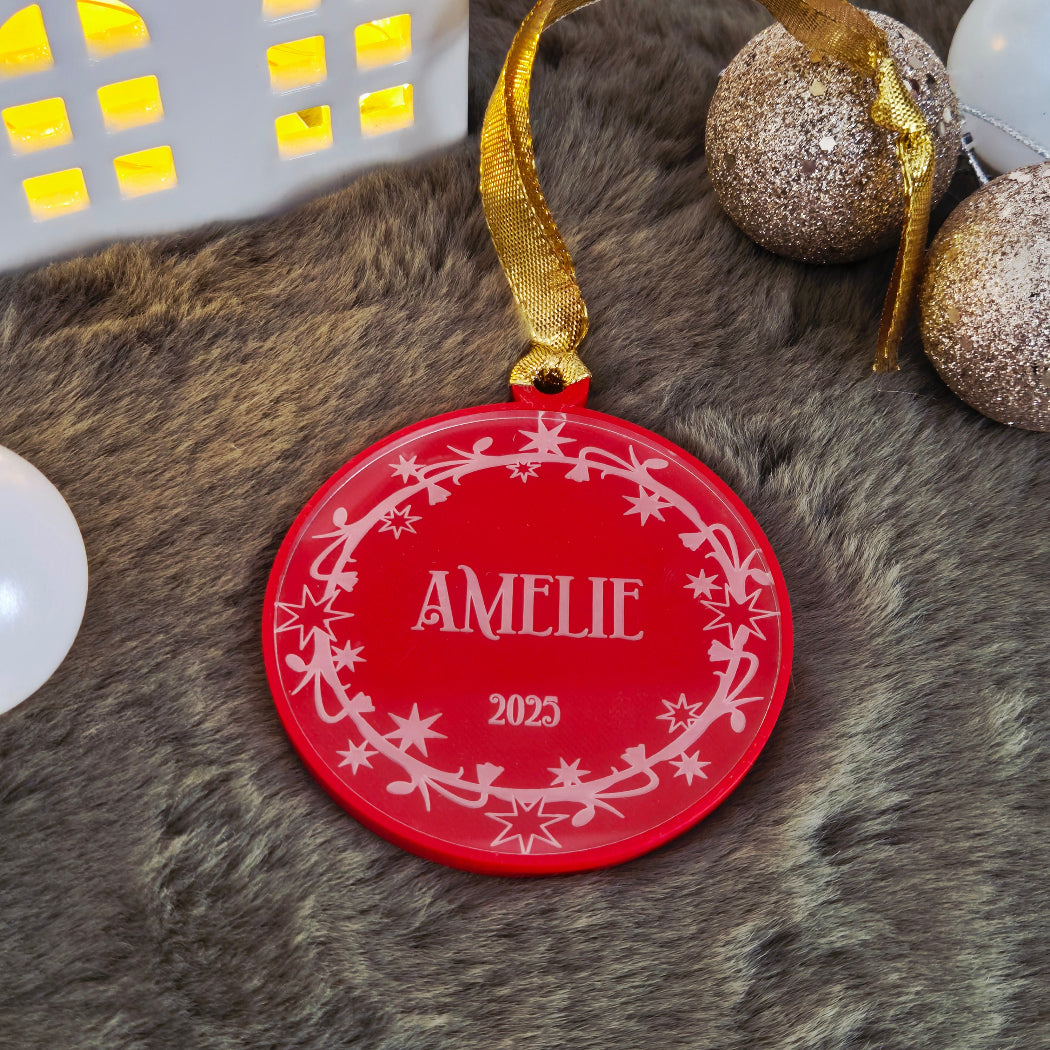 Red ornament with 'name' and '2025' on a textured surface with Christmas decorations.