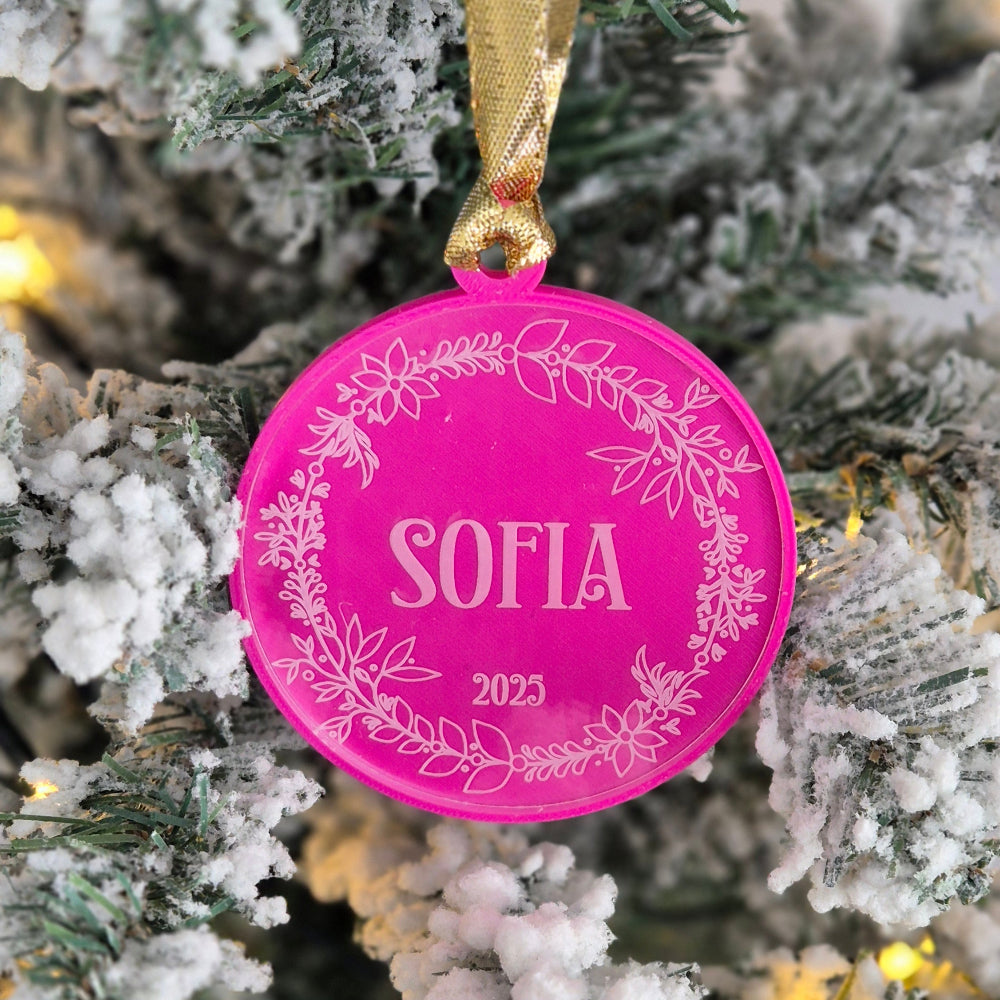 Pink Christmas ornament with 'SOFIA' and '2025' on a decorated tree.