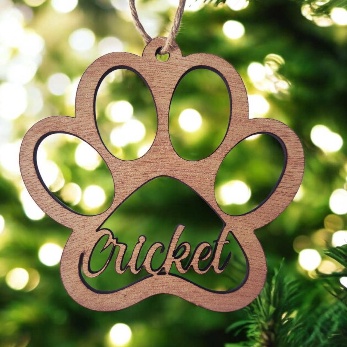 Wooden paw-shaped ornament with 'Cricket' engraved, hanging on a Christmas tree.