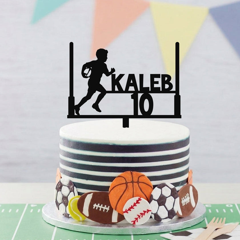A custom black sports cake topper featuring a running football player silhouette, the name 'KALEB', and the number '10', displayed on top of a decorated birthday cake with football-themed decorations.