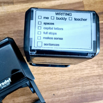Trodat Printy 4927 Writing Feedback Stamp with customizable text plate and pre-designed checkboxes for writing elements like spaces, capital letters, full stops, makes sense, sentences. The stamp is self-inking and has a transparent positioning window.
