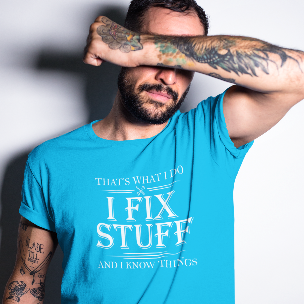 tattooed-man-covering-his-face-while-wearing-a-t-shirt that says I fix stuff and know things