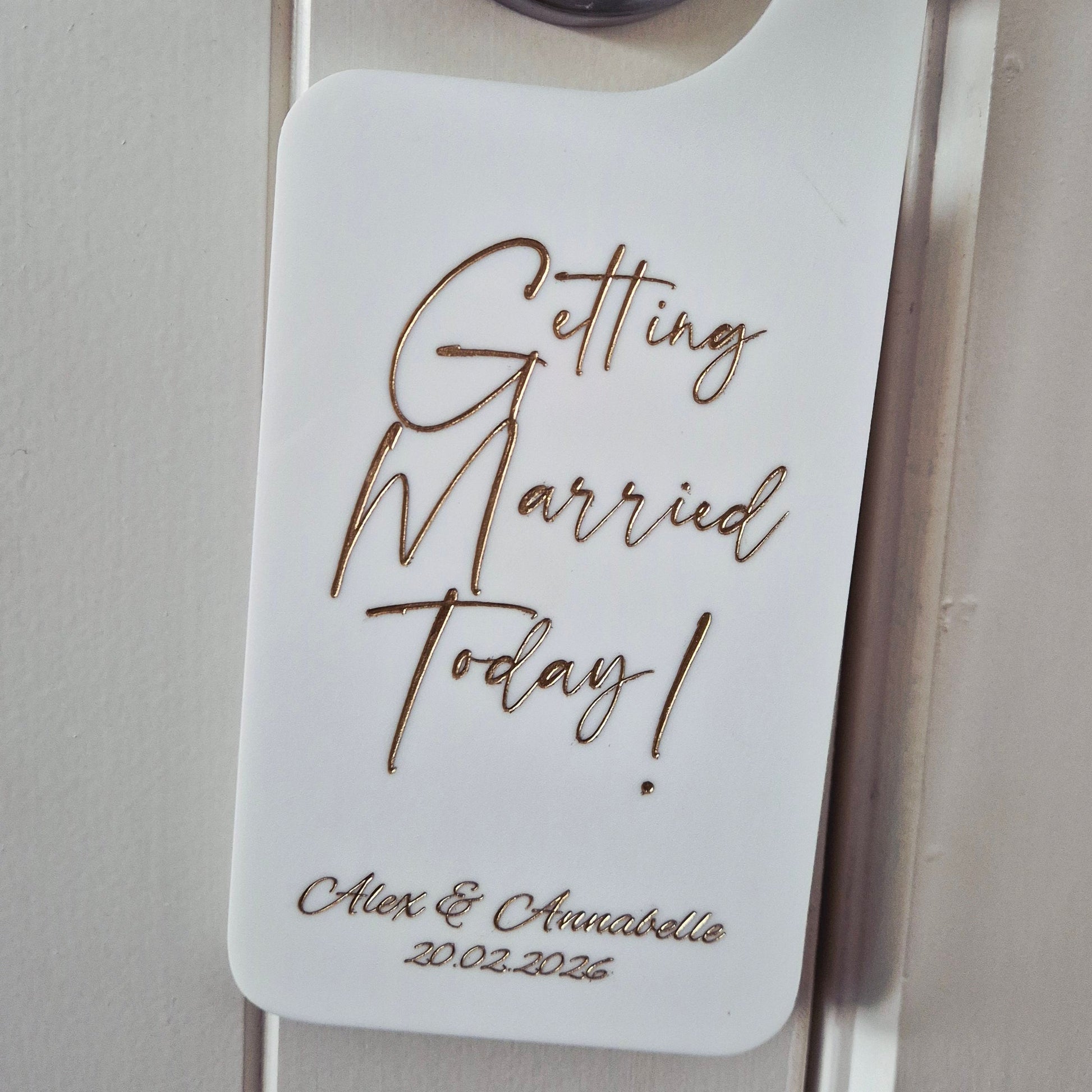 A white hanger tag with a black handle attached, printed with the words 'Getting Married Today!' in cursive and the names 'Olivia & Christopher 2022.02.