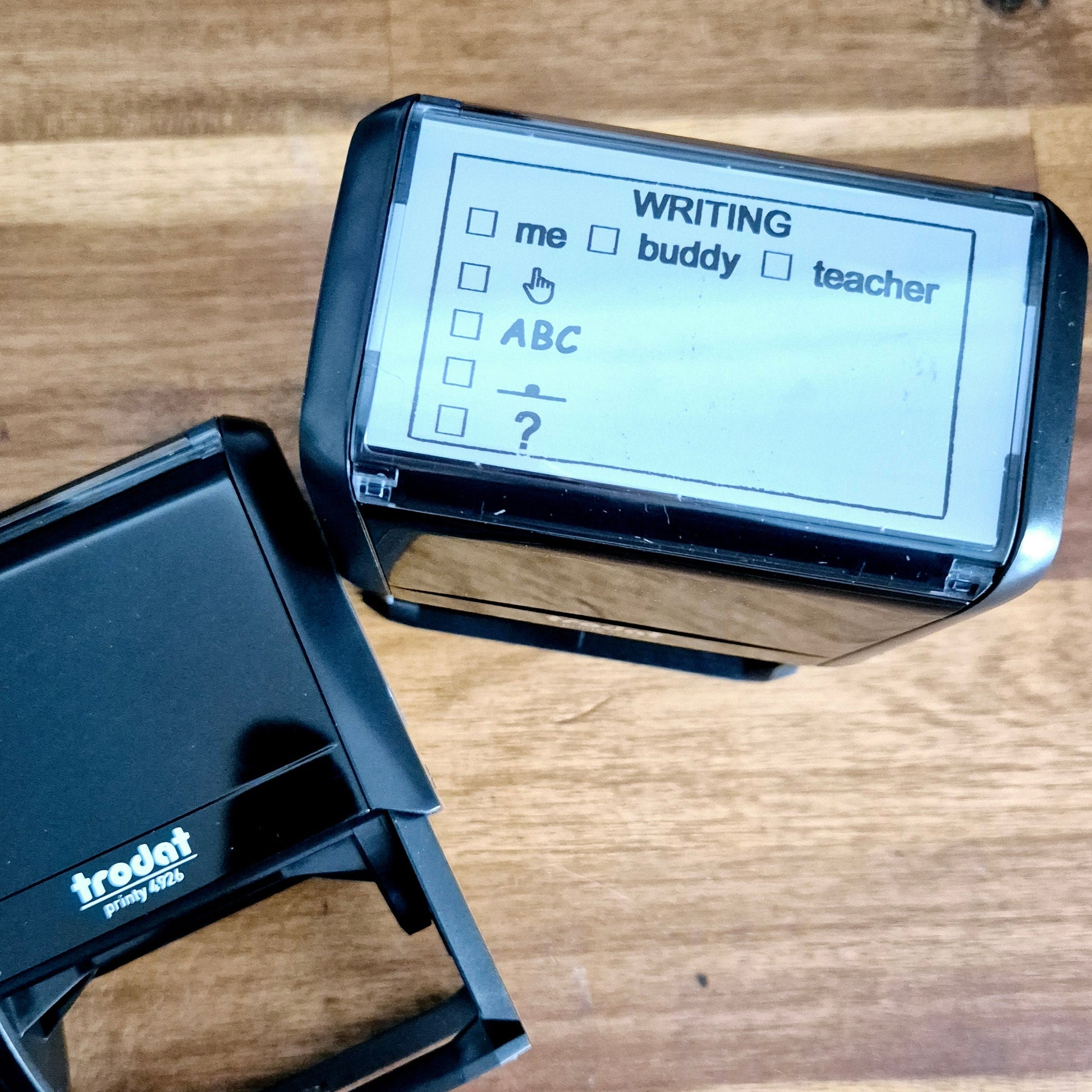 Trodat Printy 4926 Writing Feedback Stamp with custom text on a clear index window, showing options such as 'me,' 'buddy,' and 'teacher', and a question mark.