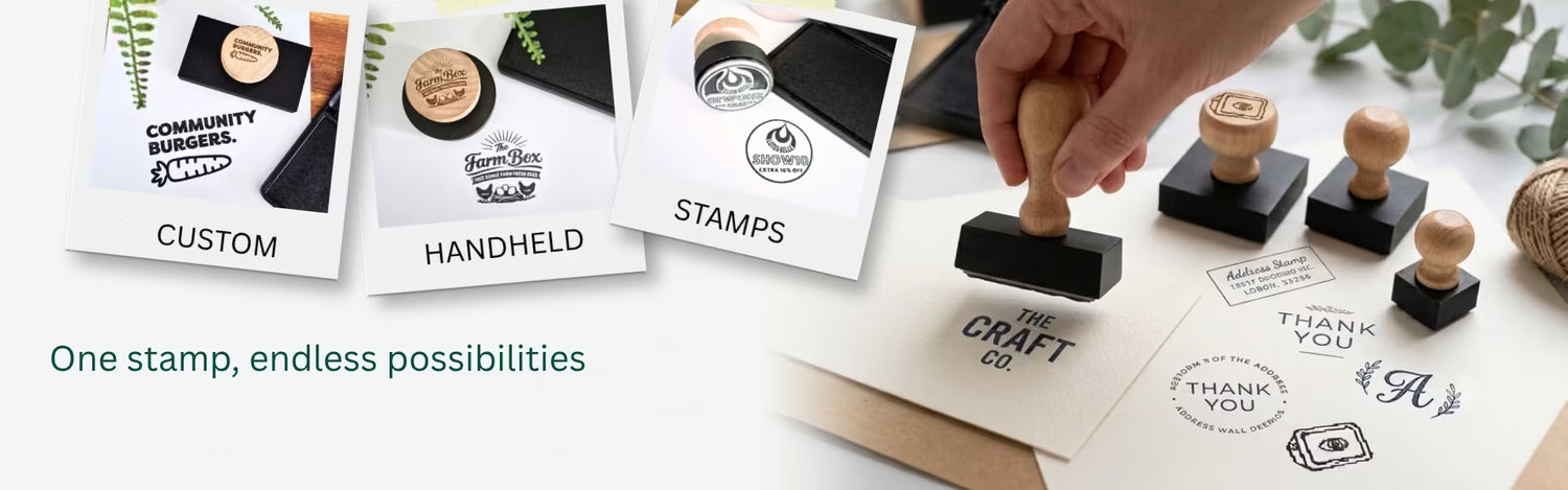 A hand is using a wooden-handled rubber stamp on a white surface, with several sample stamp designs and cards displayed nearby. The scene includes text such as 'CUSTOM,' 'HANDHELD,' 'STAMPS,' and 'One stamp, endless possibilities,' suggesting a craft stamp product shown in use.