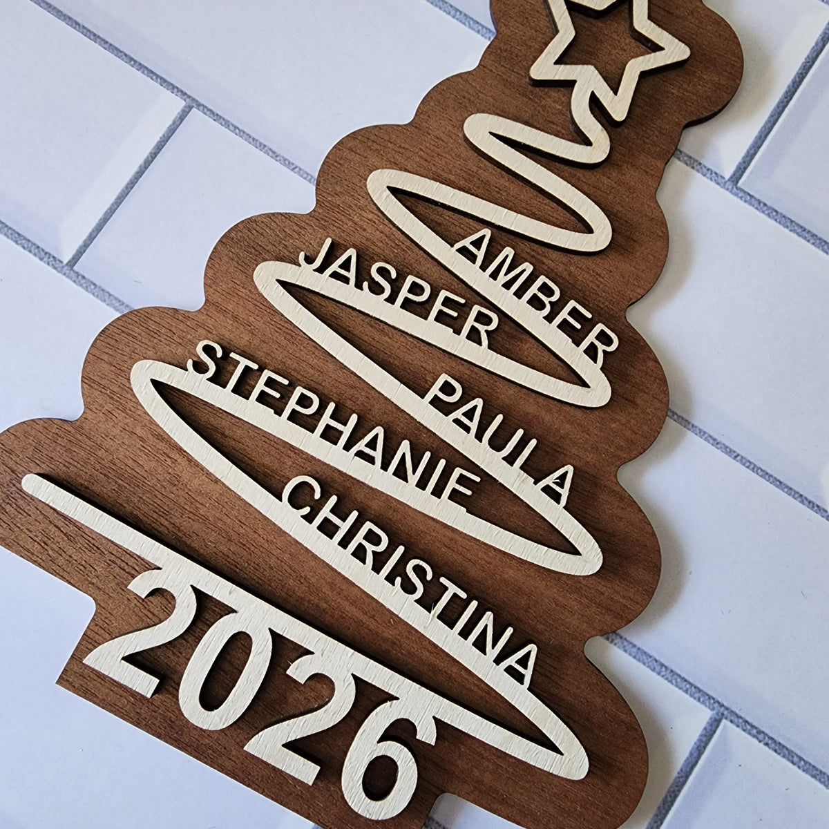 Personalised wooden family Christmas tree decoration with custom names and year 2026 hanging with red striped ribbon